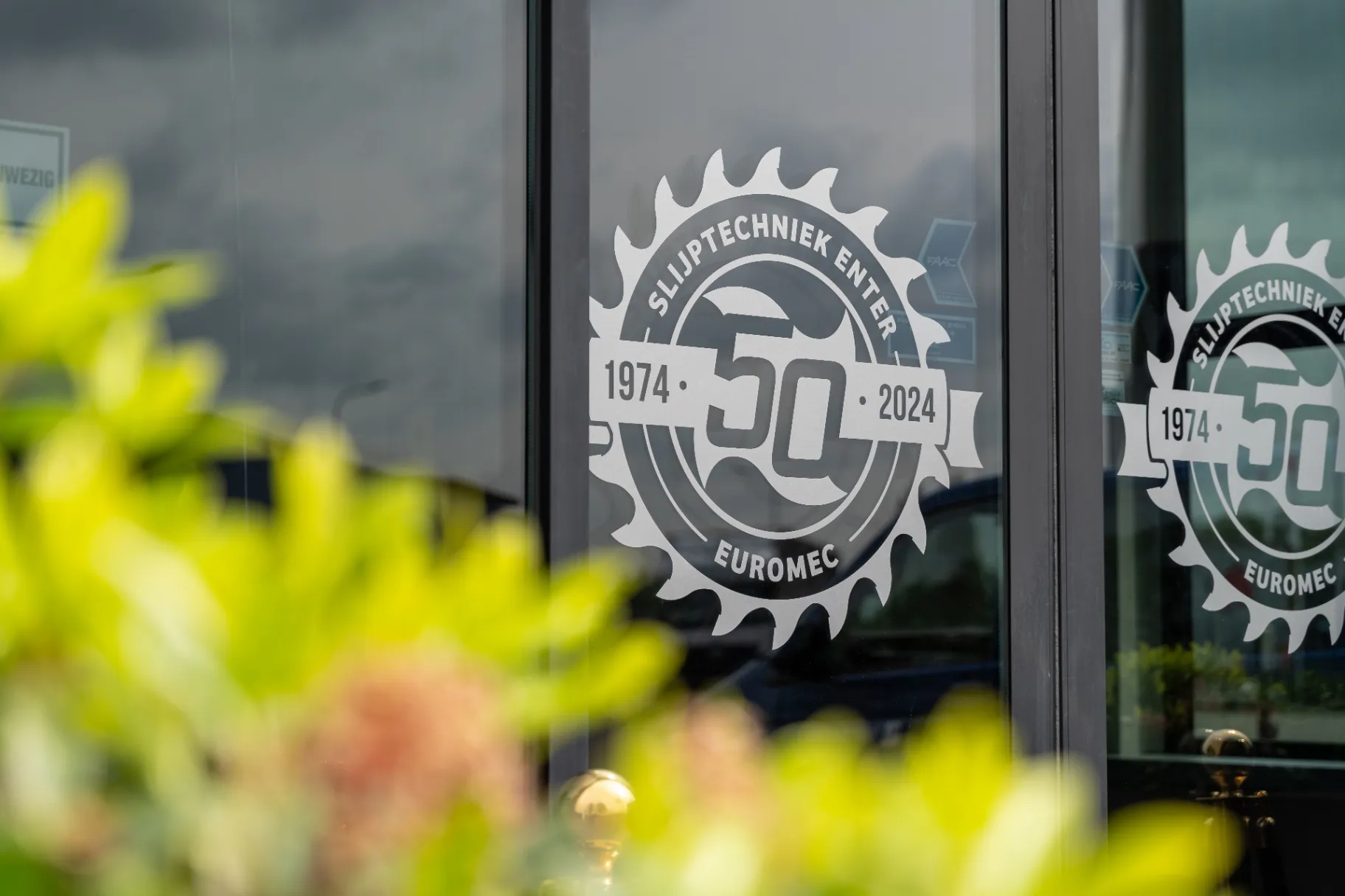Jubileumlogo van Slijptechniek Enter en Euromec, 1974 tot 2024, in de glazen entree van het bedrijfspand